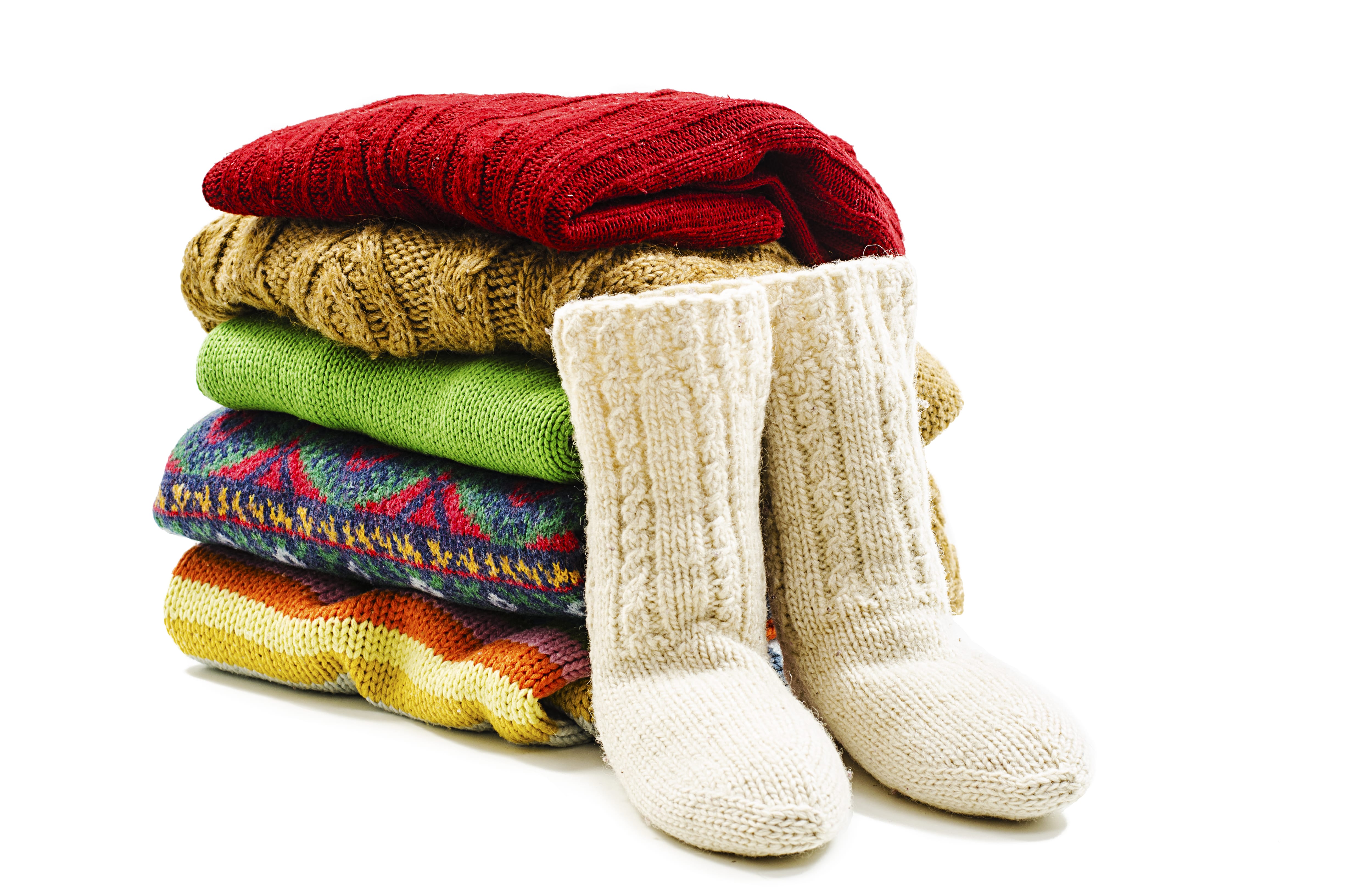 A neat pile of colorful sweaters sit next to a pair of cozy wool slippers, ready to be prepped for winter storage.